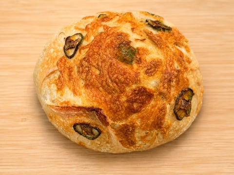 A round sourdough loaf studded with melted cheddar and jalapeño on top